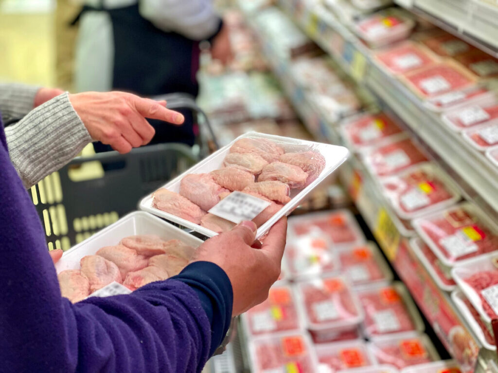 スーパーの精肉売り場で白い食品トレー入りの商品を選ぶ手元